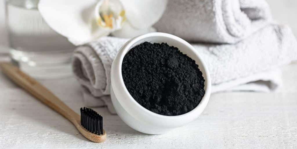 A bowl of black powder beside a bamboo toothbrush