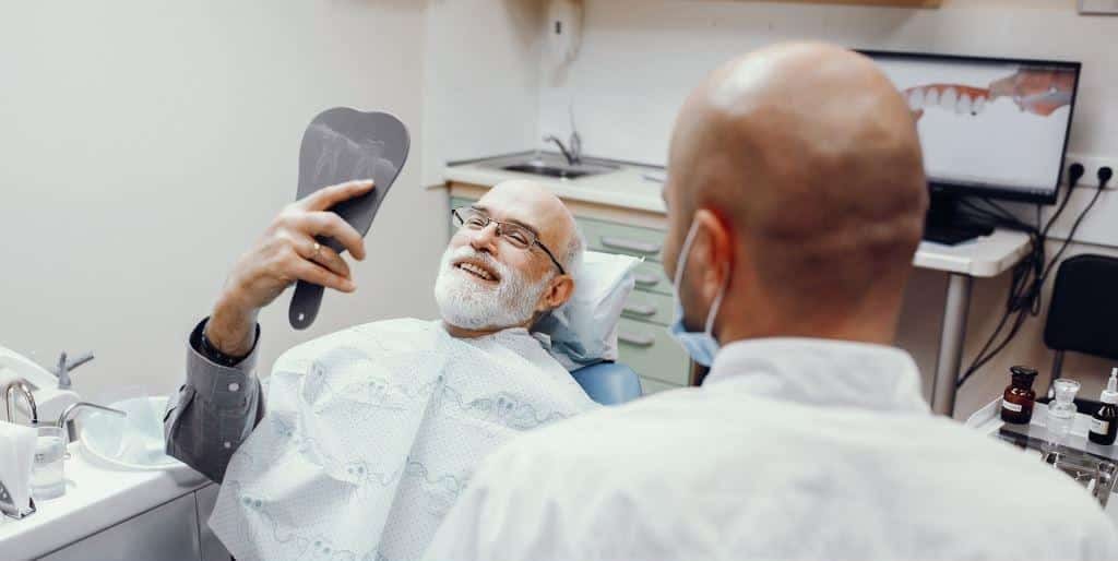 A patient looking in a handheld mirror during a dental visit