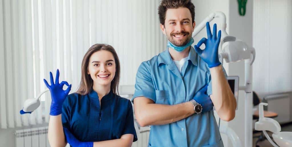 Two dental team members wearing blue uniforms and gloves