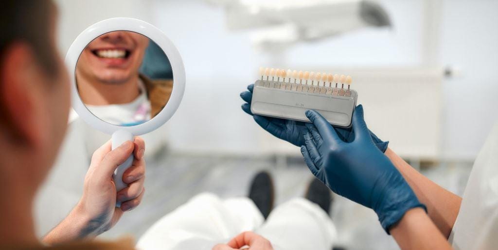 A patient looking in a mirror beside a tooth shade guide