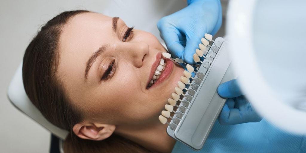 A tooth shade guide held beside a patient’s teeth