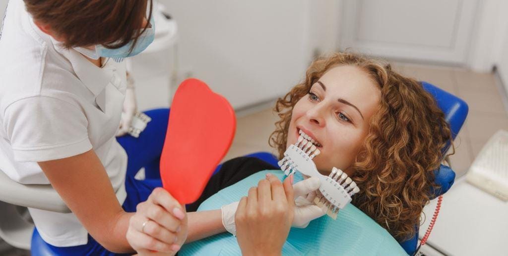 A patient holding a mirror while a clinician compares tooth shades