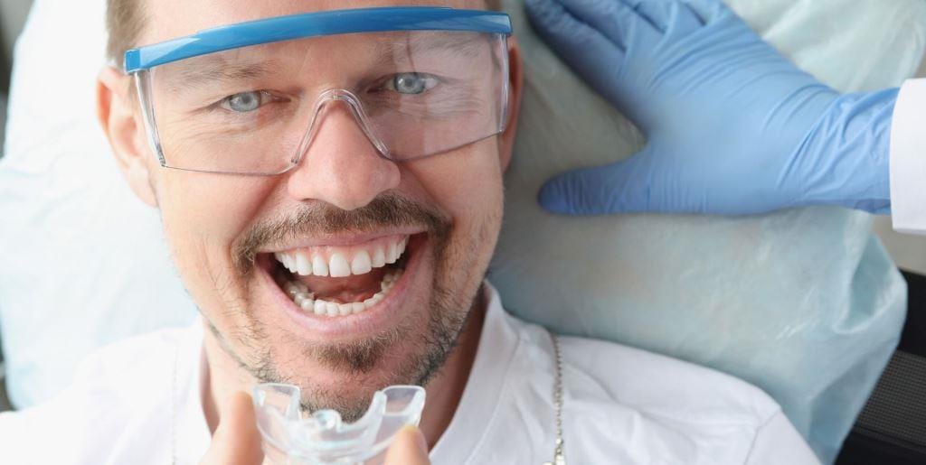 A smiling patient wearing protective glasses in a dental chair