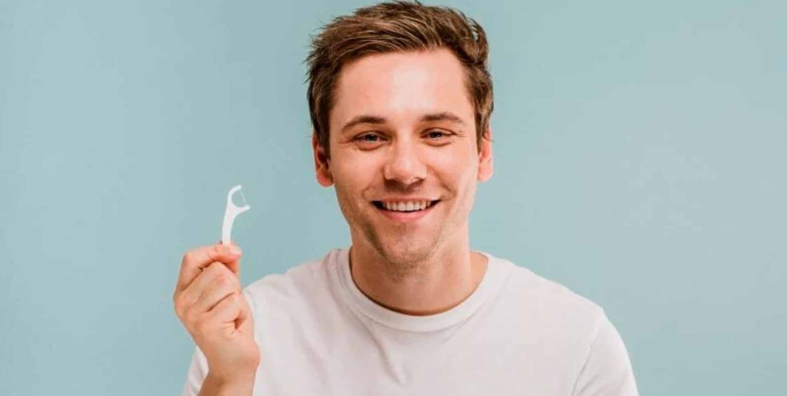 A smiling man holding a floss pick