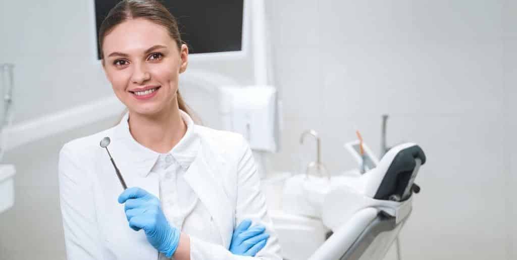 A dental professional holding a mouth mirror beside a dental chair
