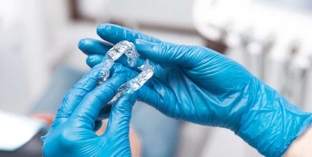 Gloved hands holding clear aligners