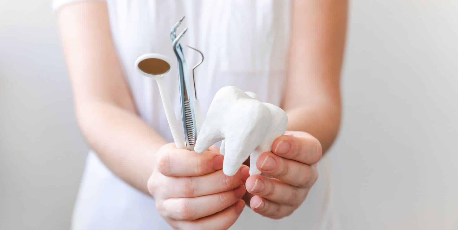 Hands holding dental instruments and a model tooth