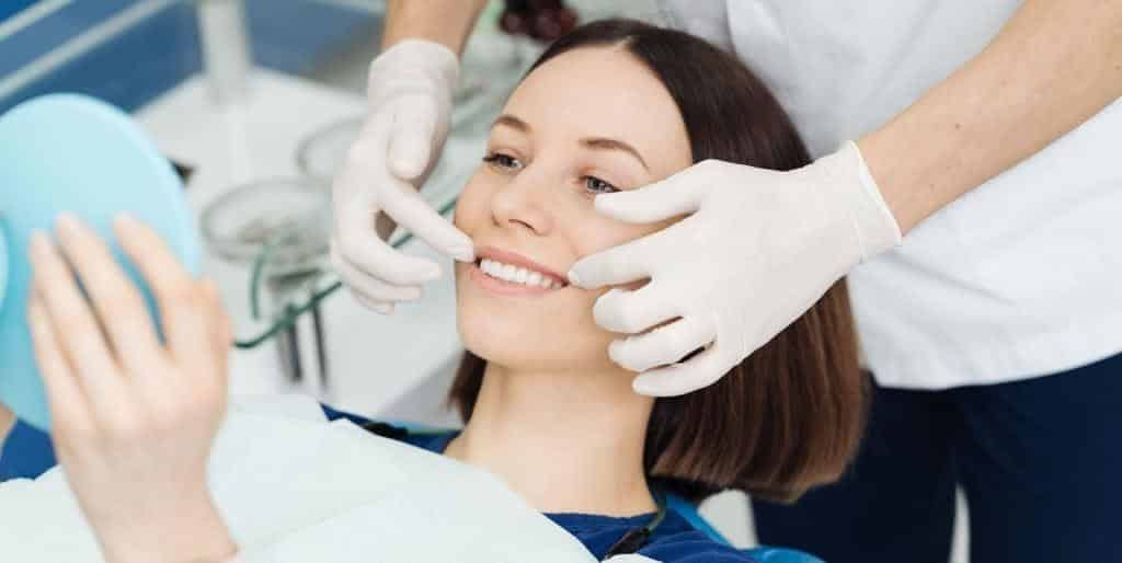 A patient looking in a hand mirror during a dental examination