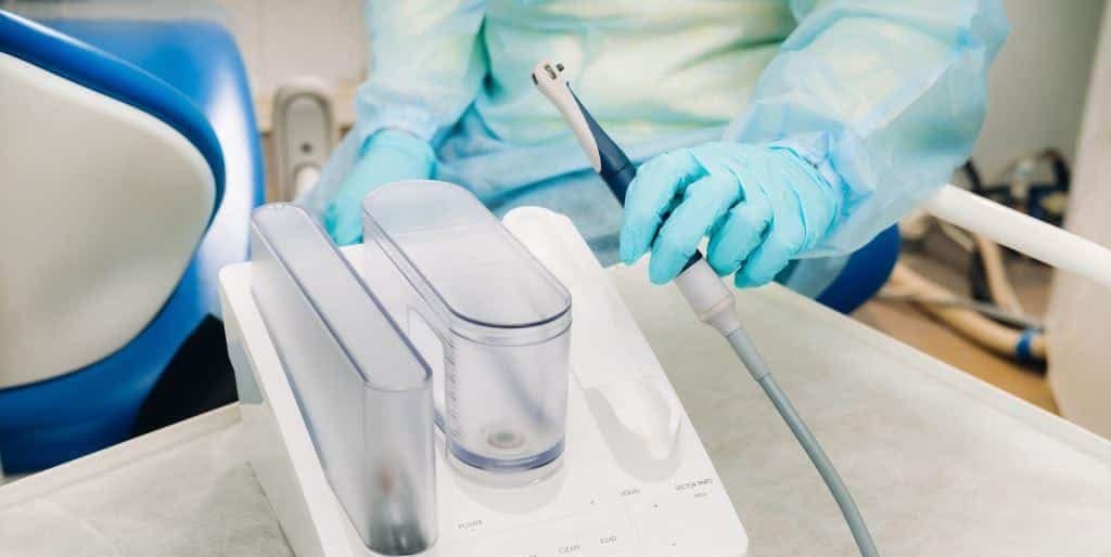 Gloved clinician holding a dental instrument beside the dental unit