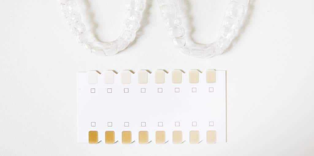 Clear dental trays beside a tooth-colour chart