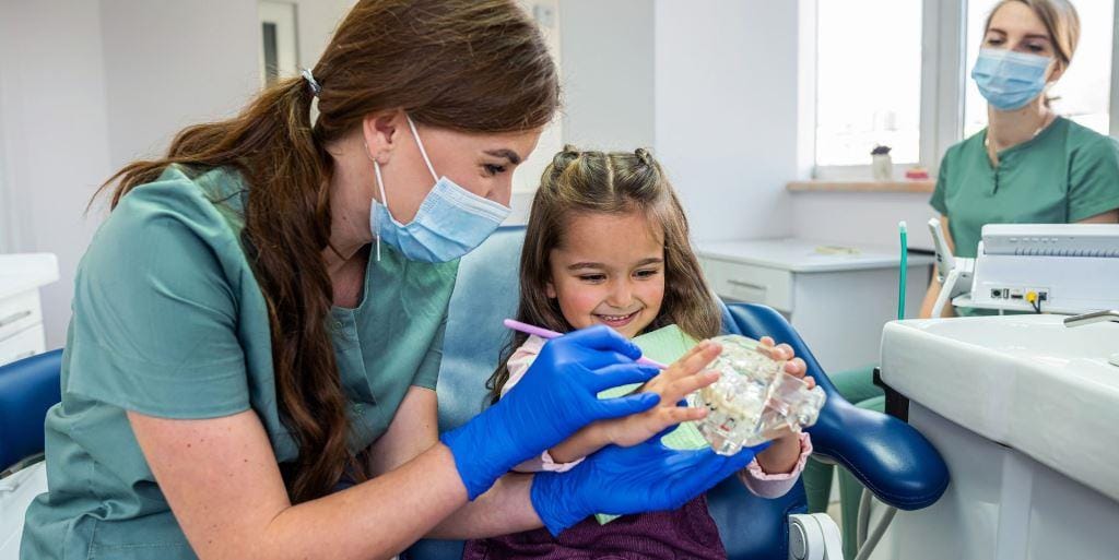 Dental professional showing a child how to brush a tooth model