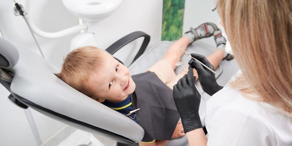 Child in a dental chair looking at a dental instrument