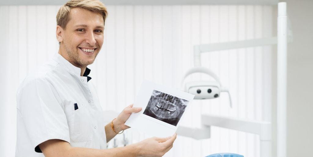 A smiling dentist holding a dental X-ray