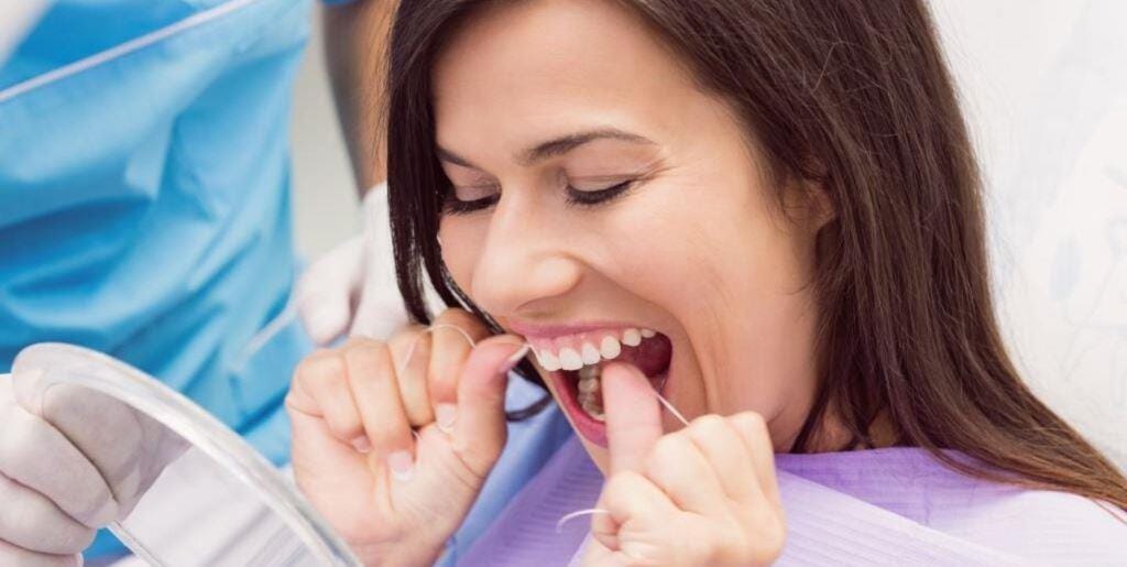 A patient using dental floss while holding a mirror