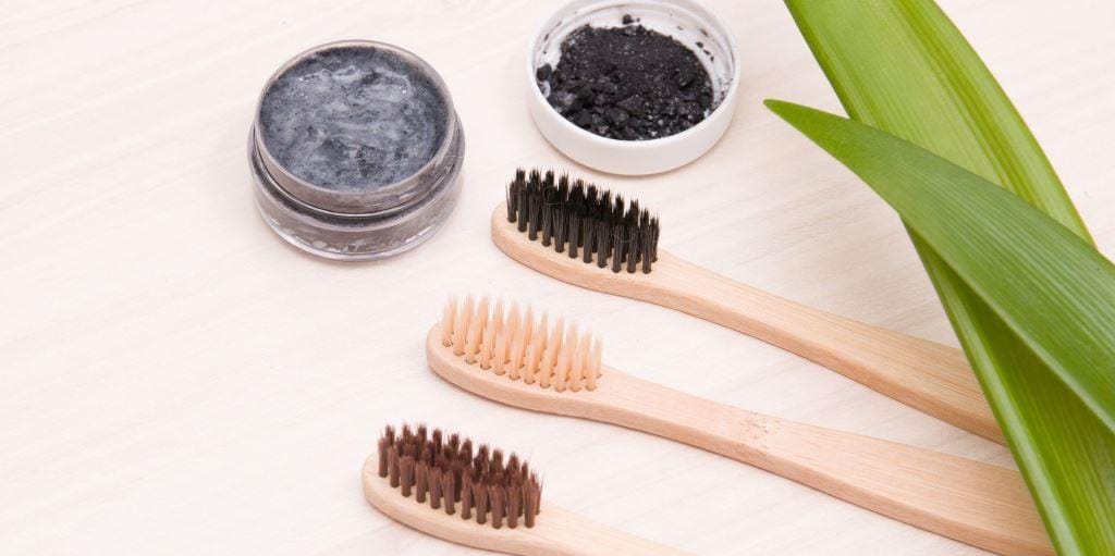 Wooden-handled toothbrushes beside containers of dark powder