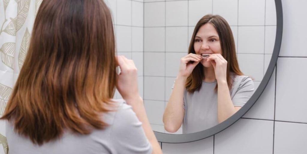 A woman fitting a clear dental tray while looking in a mirror