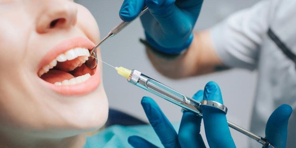 A dentist holding a dental syringe beside a patient’s mouth