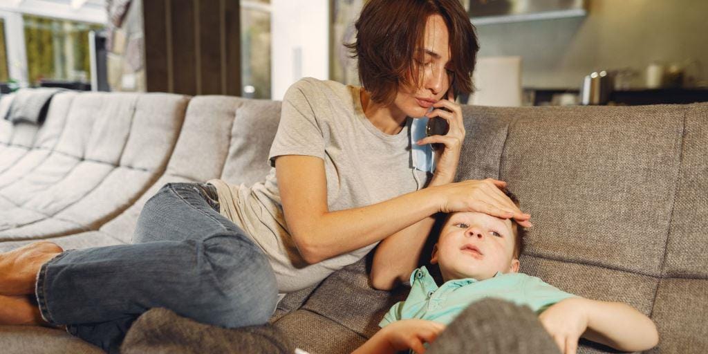 Parent using a phone while checking a child’s forehead