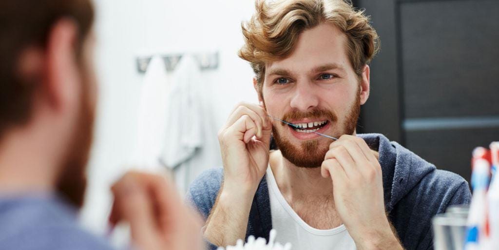 A man using dental floss in front of a mirror