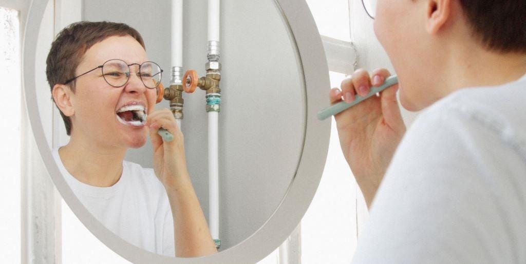 A person brushing their teeth in front of a bathroom mirror