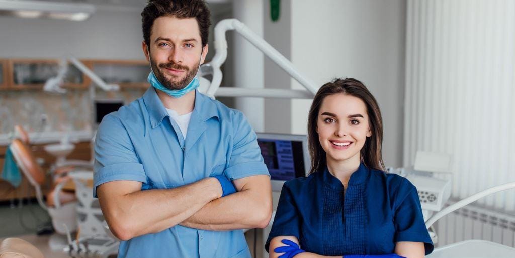 Two people in dental uniforms beside a treatment chair