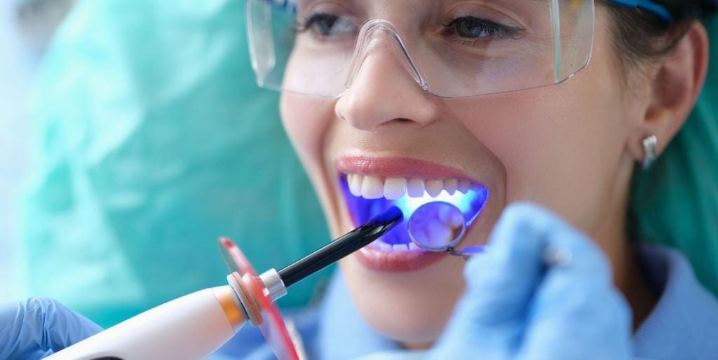 A dental curing light being used on a patient’s front teeth