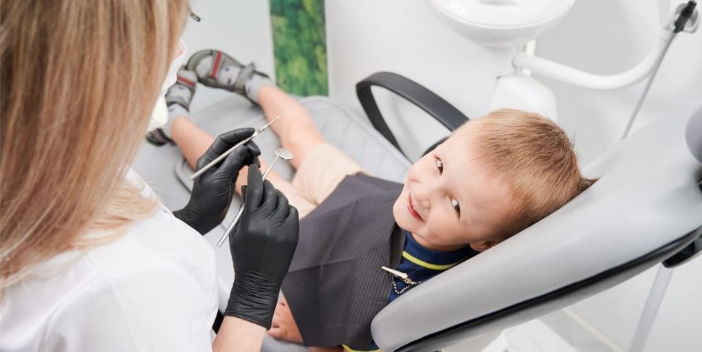 A child looking towards a dental team member holding instruments