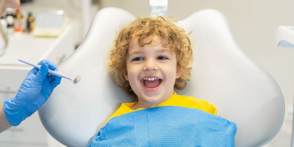 A child smiling in a dental chair beside a dental mirror