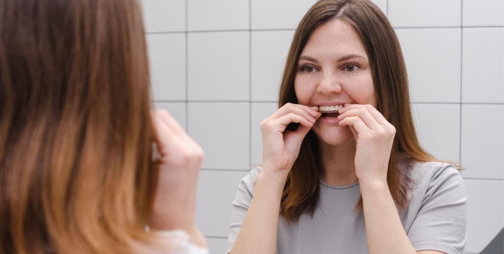 A woman fitting a clear dental tray while looking in a mirror