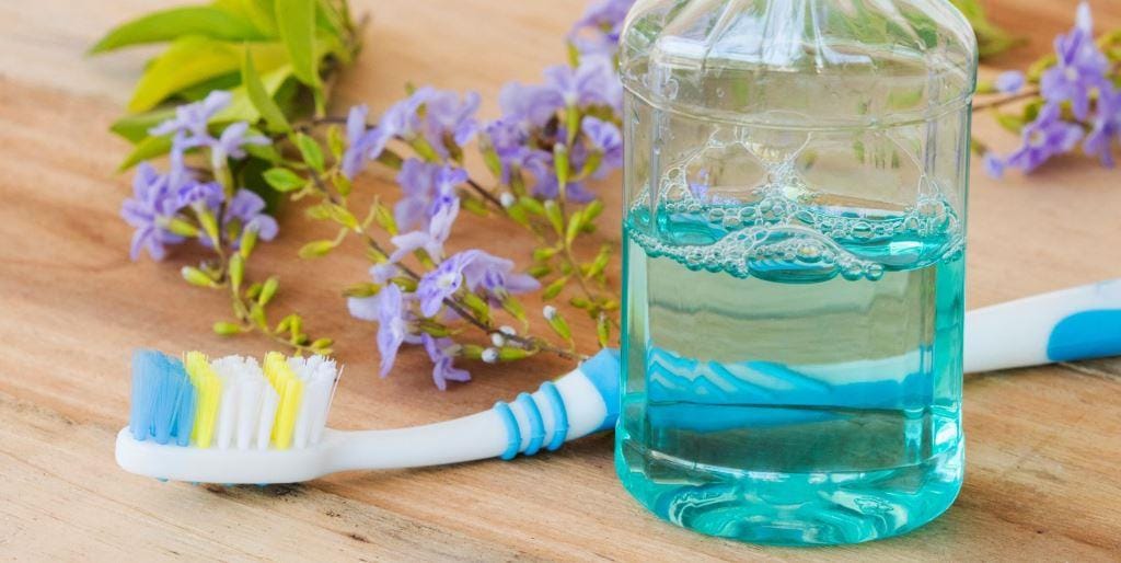 A toothbrush, a glass of blue liquid and a bottle beside flowers