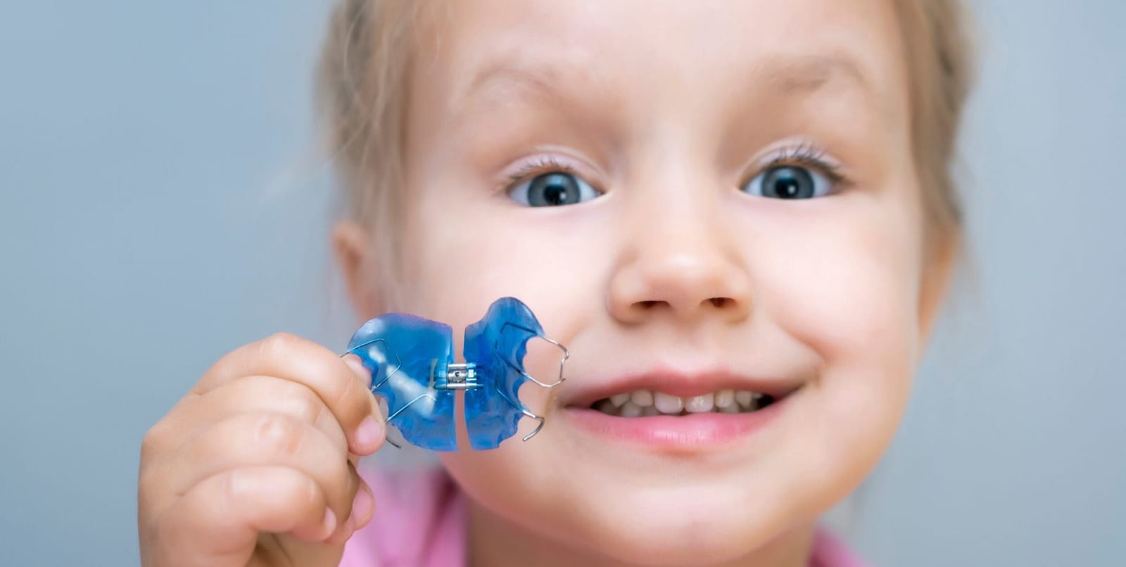 Child holding a blue removable orthodontic appliance
