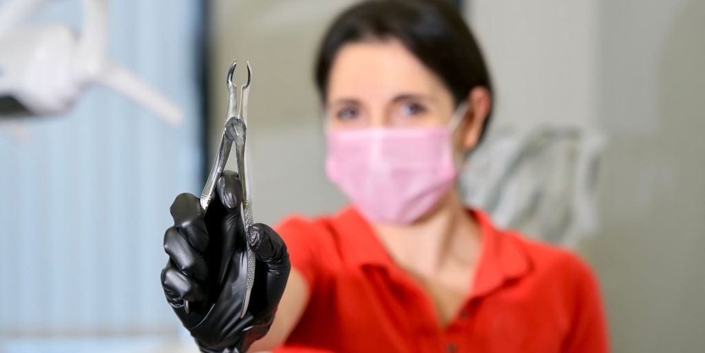 A masked clinician holding dental forceps