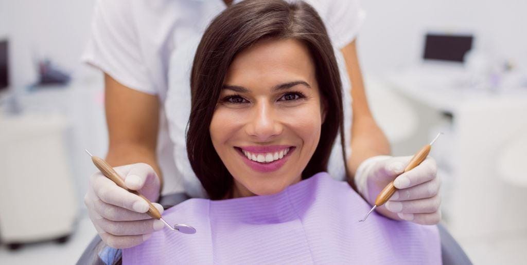 A patient wearing a purple bib, with a dentist holding instruments nearby