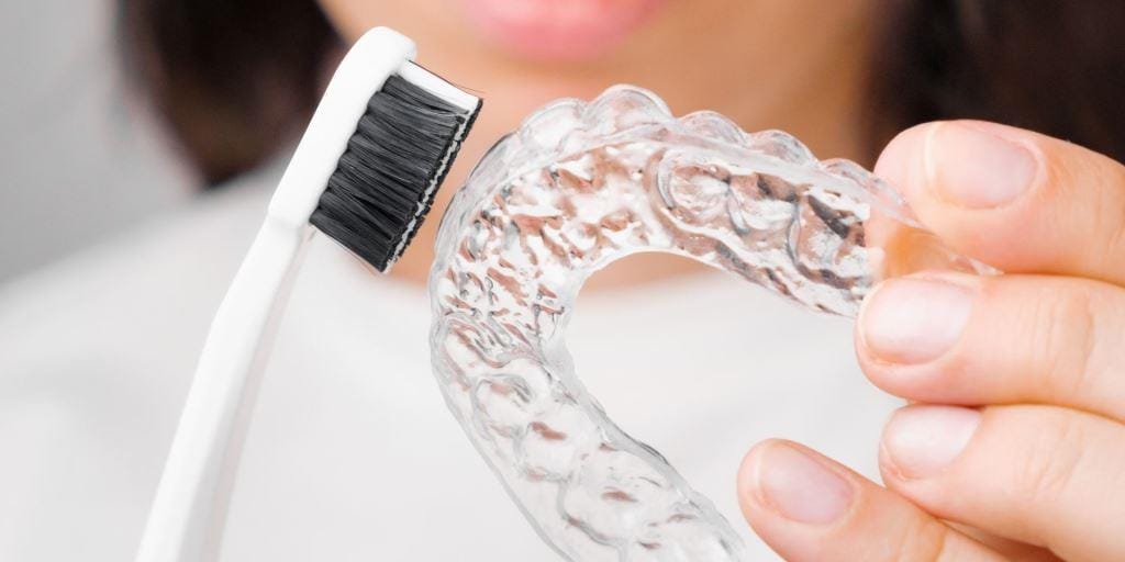 A clear removable dental appliance held beside a toothbrush