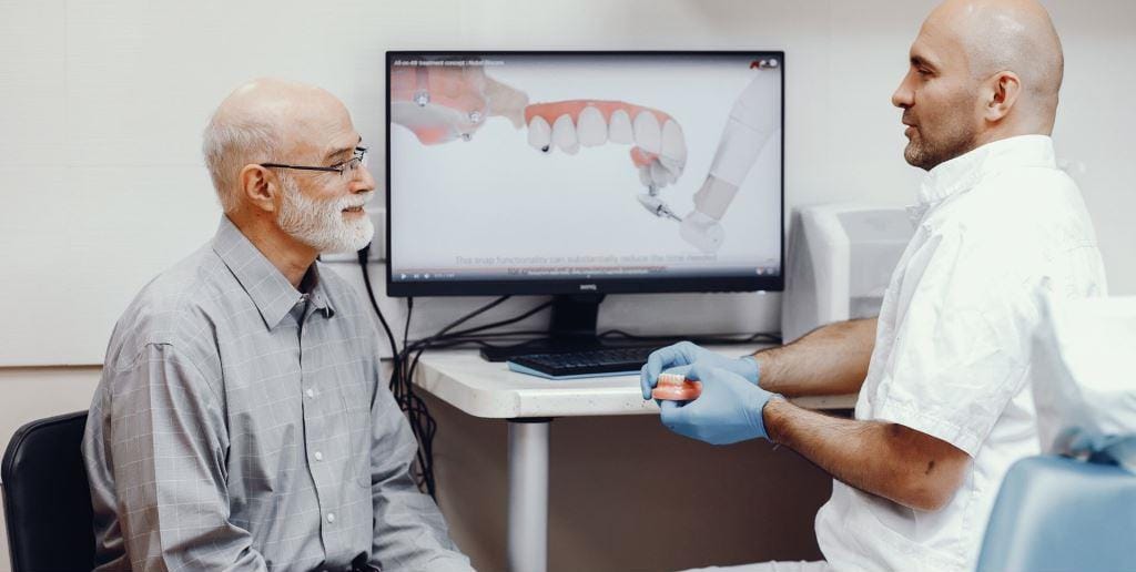 A patient and clinician discussing a dental model on a screen