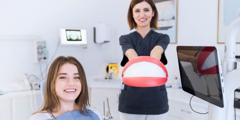 Dental team member holding a model of teeth beside a patient