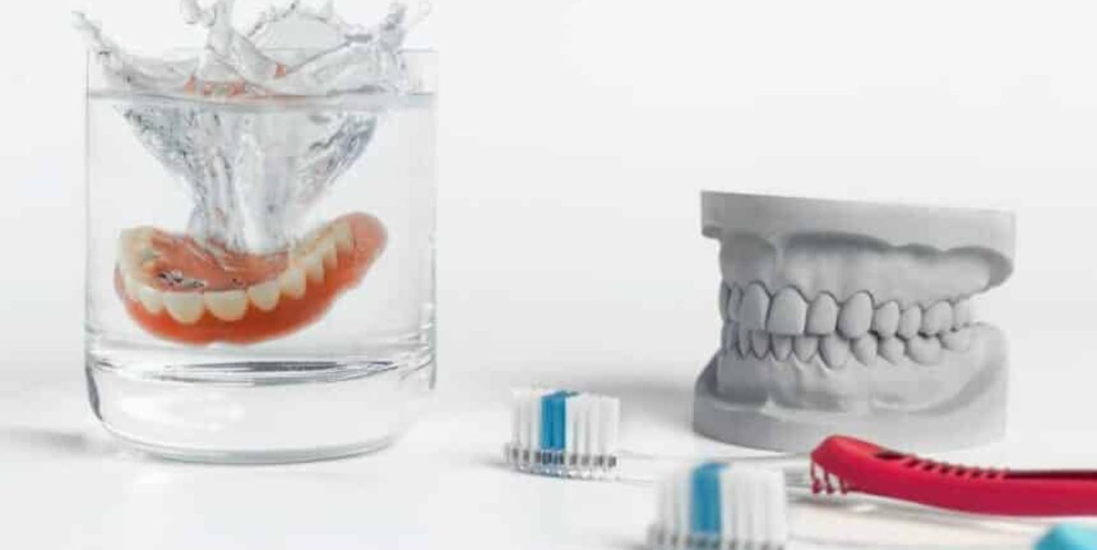 A denture in water beside a dental model and toothbrushes