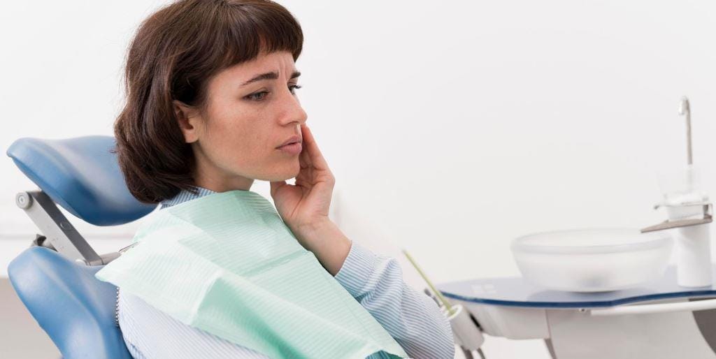 Patient touching her cheek while seated in a dental chair