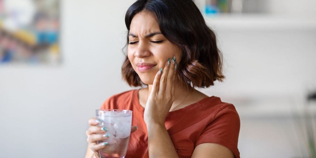 A woman holding a glass of water and touching her cheek