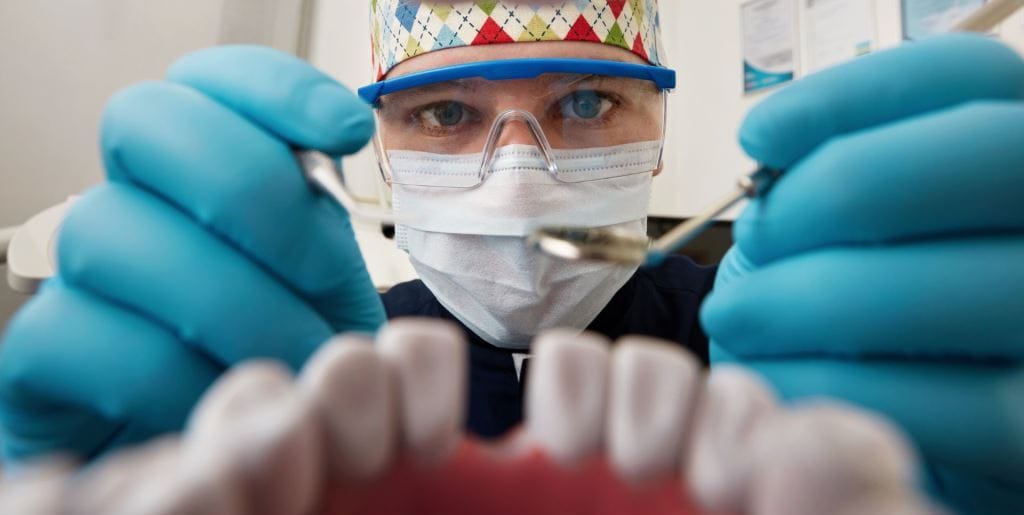 A clinician wearing a mask and gloves and holding a dental instrument