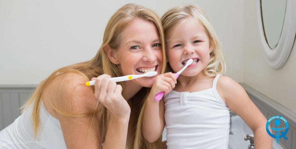 An adult and a child brushing their teeth together