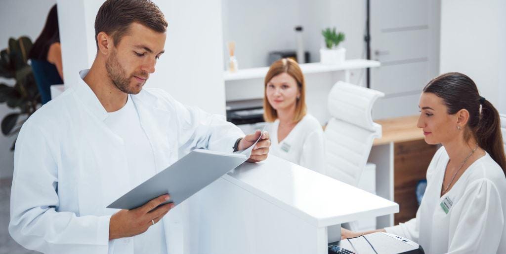 Three people in a clinical reception area reviewing paperwork