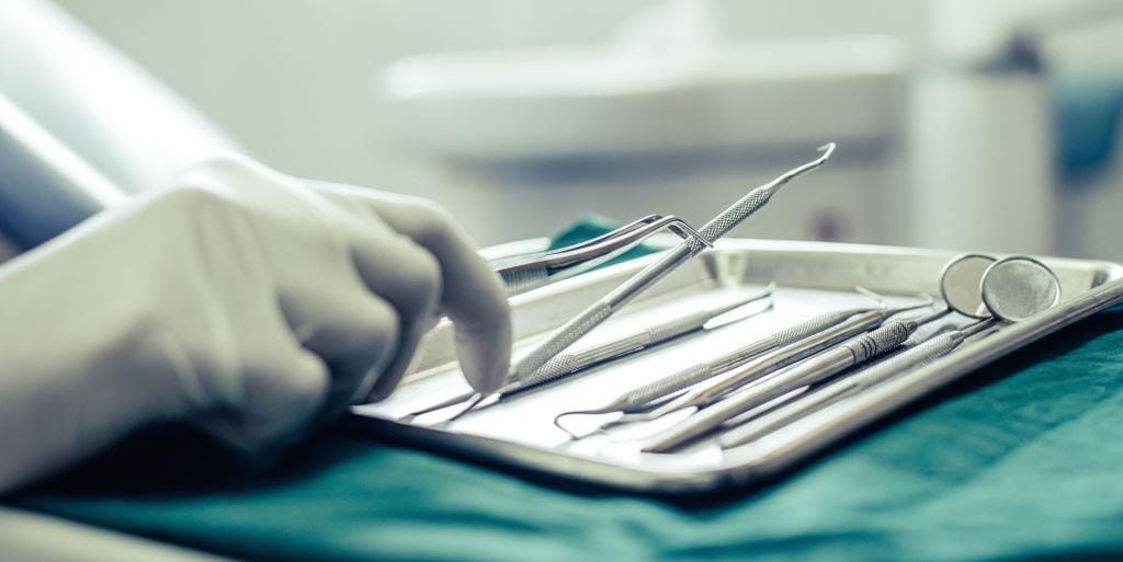 Dental instruments on a tray beside a gloved hand