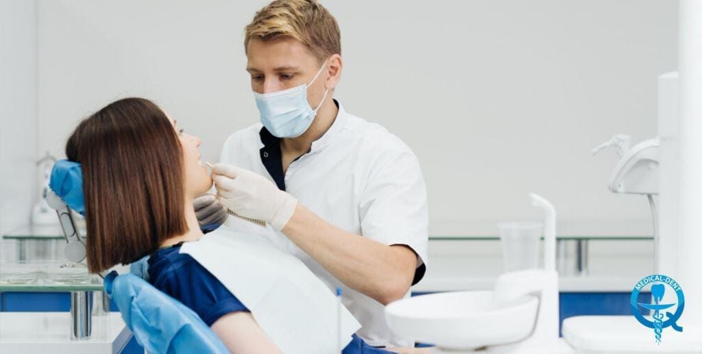 A masked clinician examining a patient in a dental chair