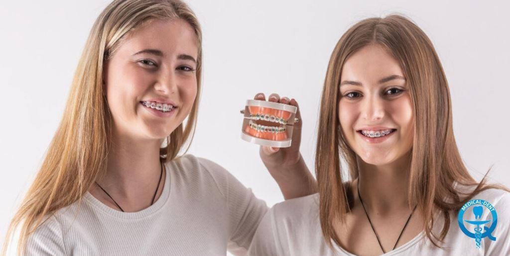 Two people wearing braces, with one holding a dental model