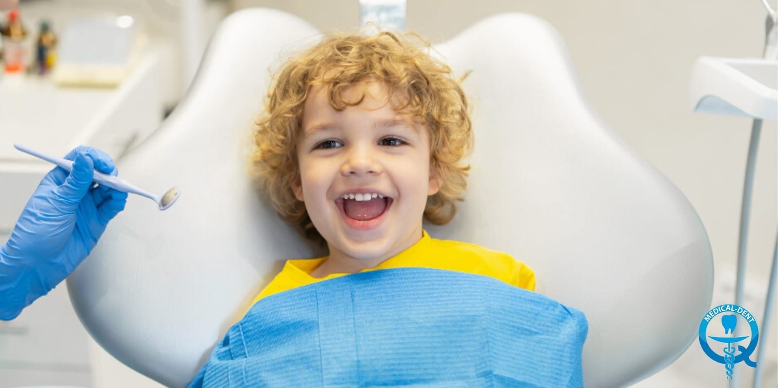 A child sitting in a dental chair beside a dental mirror