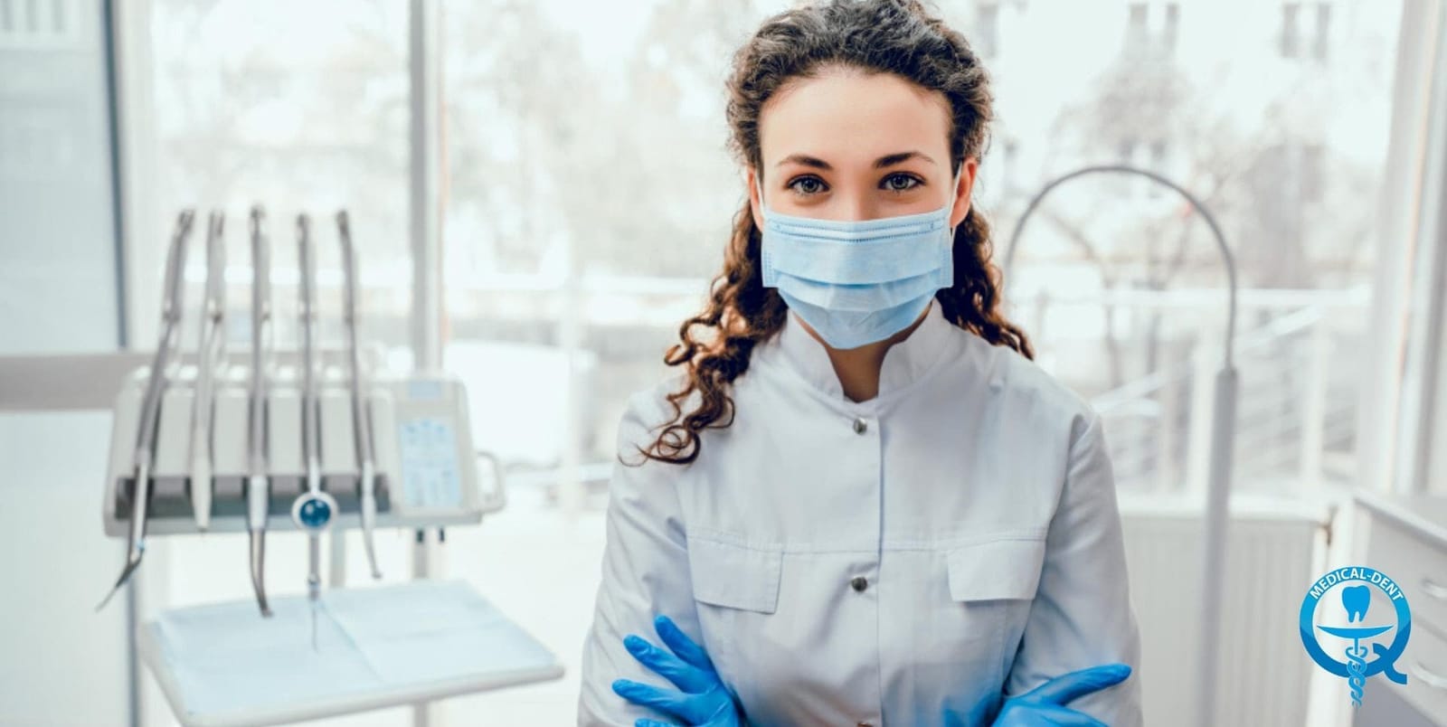 A masked dental clinician standing beside dental equipment