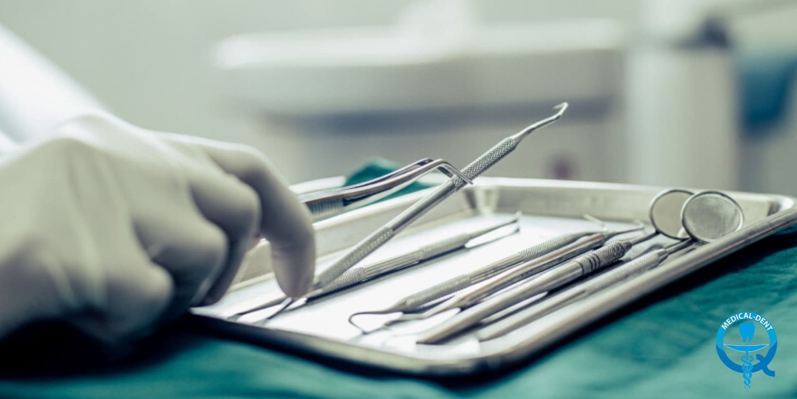 Dental instruments arranged on a tray beside a gloved hand