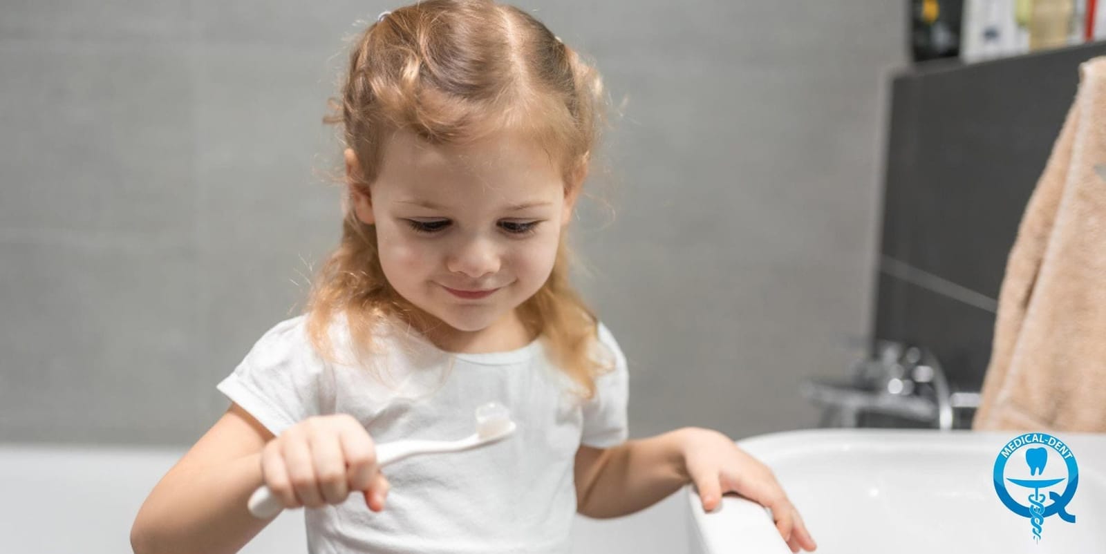 A child holding a toothbrush by the bathroom sink.