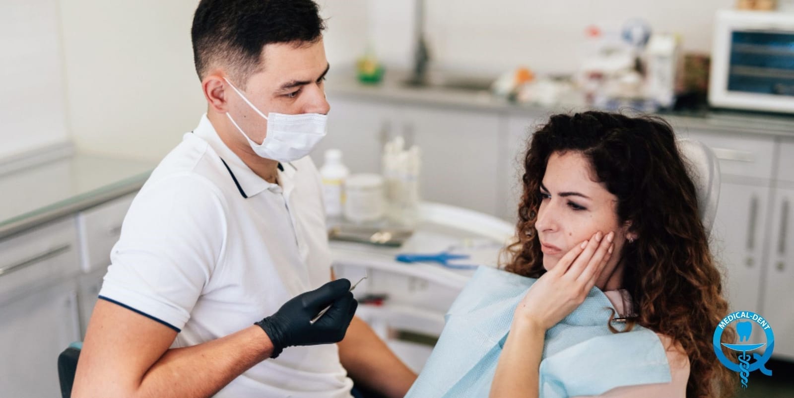 A masked clinician talking to a patient who is holding her cheek